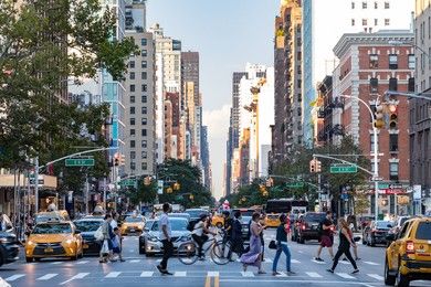 NEW YORK CITY - CIRCA 2017: Busy crowds of people walk across 3rd Avenue in front of rush hour traffic in the East Village neighborhood of Manhattan in New York City.