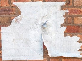 Old blank paper pasted on a wall torn in places dirty with corners edges curling away from surface