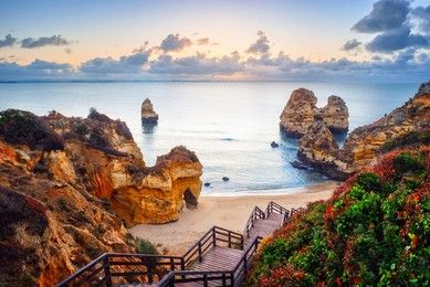 beautiful Atlantic ocean view horizon with sandy beach,  rocks and waves at sunrise. Algarve,  Portugal