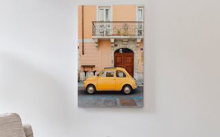 A canvas print of a small yellow car above a side table.