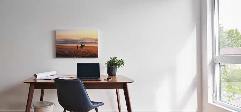 A canvas print positioned above a desk with a laptop.