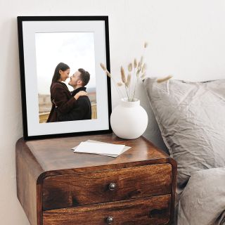 A custom framed print leaning against the wall on top of a bedside table